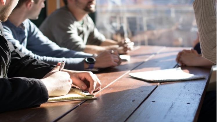 People sitting at a table taking notes on notepads discussing the benefits of account planning software.